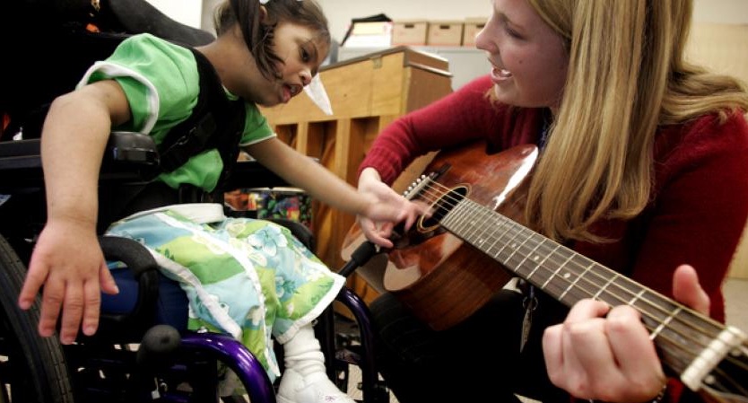 Young woman playing guitar with a child in a wheelchair